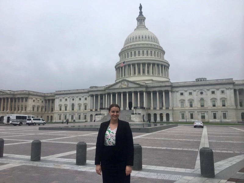 A woman dressed in a suite smiling and standing in front of the capital building