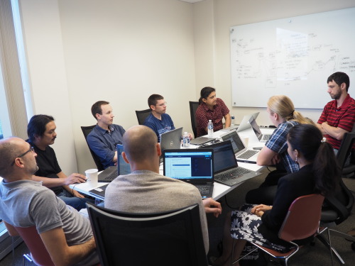 A group of people sits around a table with laptops