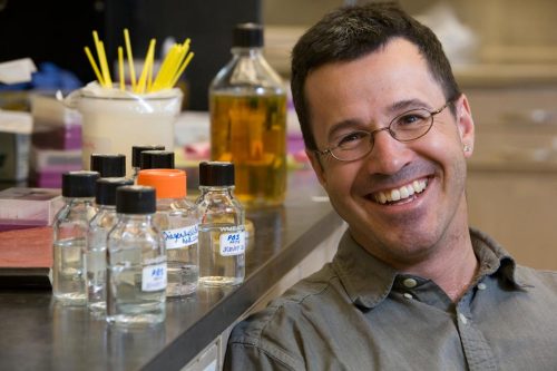 A man poses next to laboratory equipment