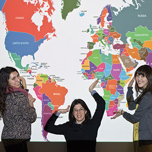 Three women pose in front of a large world map hanging on a wall