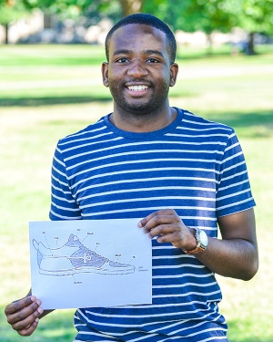 A man stands holding a paper with a drawing of a sneaker design on it