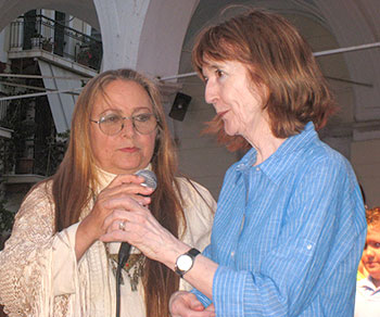 Two women stand together and talk in a microphone