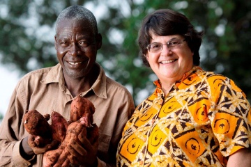 A woman and man stand together while the man holds sweet potatoes