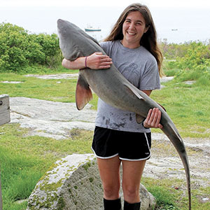 A woman holds a large shark as she stands on land
