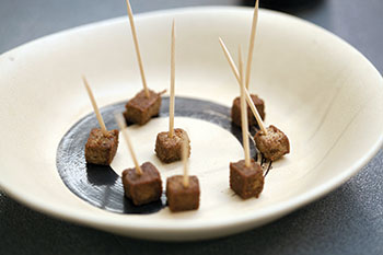 Seven mealworm squares on a plate with toothpicks in them