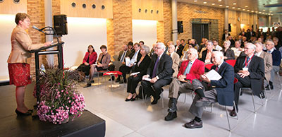 A woman speaks at a podium in front of a room full of people
