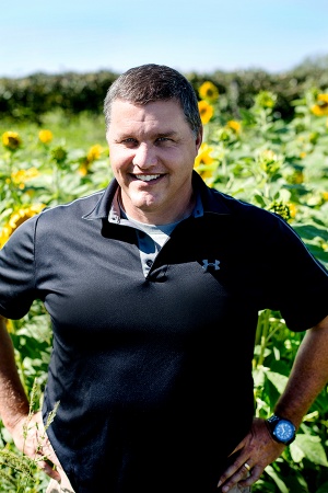 A man in a black collared shirt stands in a vineyard