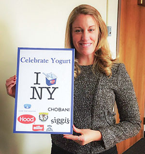 A woman holds a sign that says "I [yogurt cup] New York"