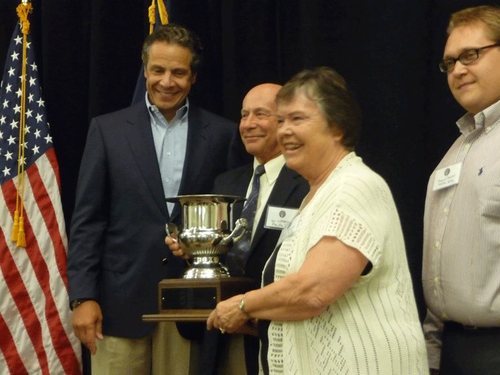 Four people stand together posing for the camera and two of them hold a trophy