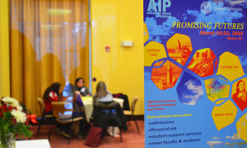 An American Indian program flyer sits on a pane of glass in focus as four women sit at a table behind it out of focus