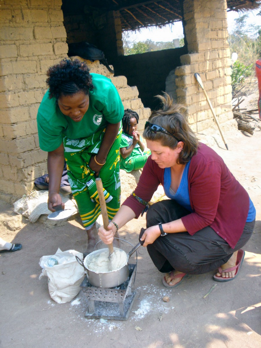 Two women bending over a bucket outside and mixing something in the bucket