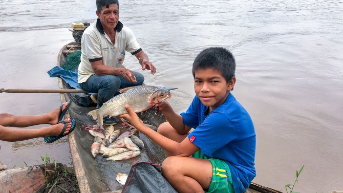 A boy holds a fish while sitting on a boat
