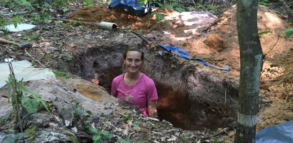 Researcher stands in a soil pit in the forest