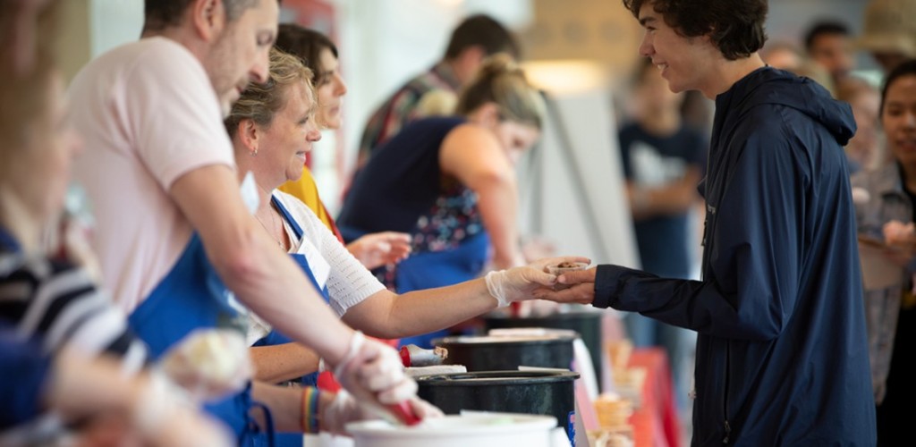 Workers scoop and hand ice cream to students