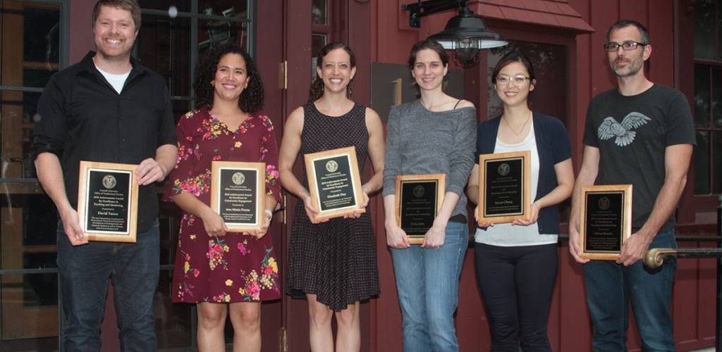 Six postdocs stand in a row holding plaques