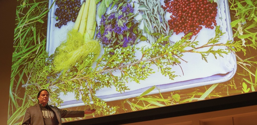 Sean Sherman stands in front of a presentation screen with food presented on it