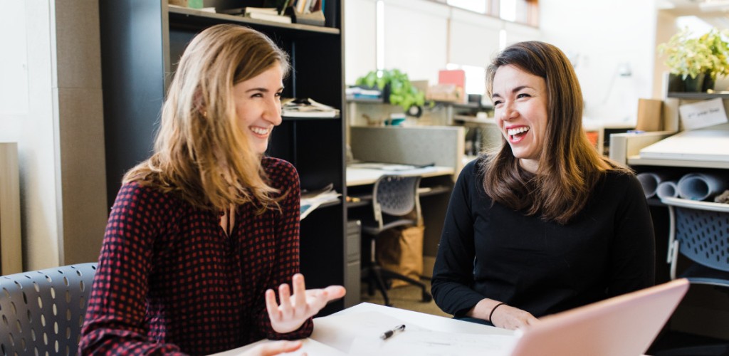 Two women laugh while sitting at a table