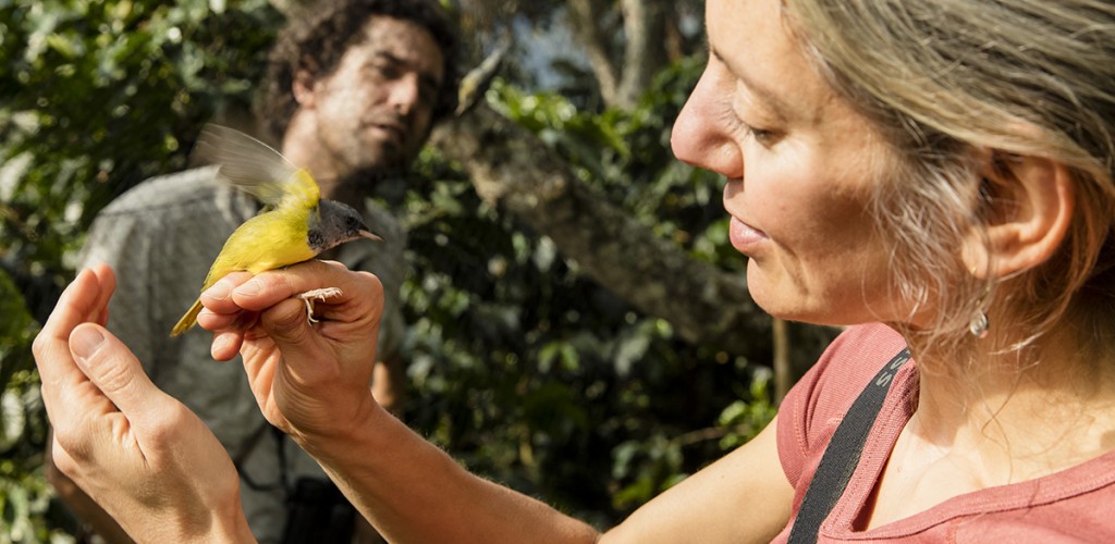 professor holds a bird in her hand while someone looks on