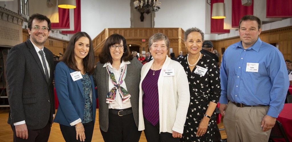A group of adults, containing two men and four women, standing together in a line smiling for the camera