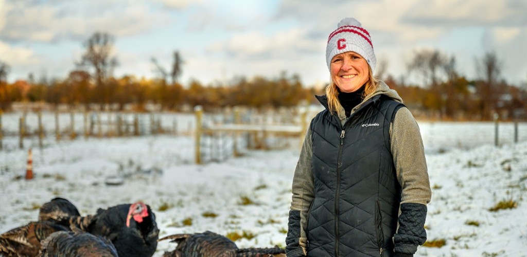 A woman standing outside in a snow-covered field with turkeys behind her