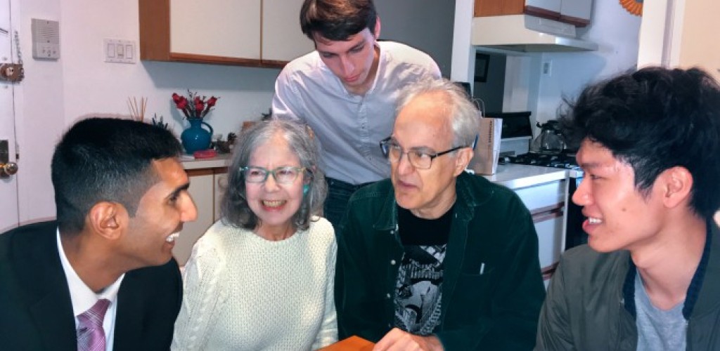 Three young men talk with an older couple around their kitchen table.