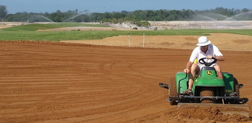 A man wearing a hat uses a piece of John Deer farm equipment in an open field