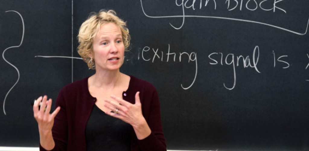 A woman stands in front of a chalkboard while teaching