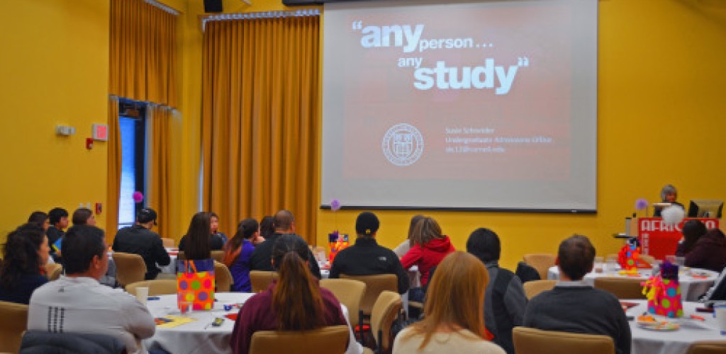 Many people sit in a room and listen to a woman speak at a podium and give a presentation