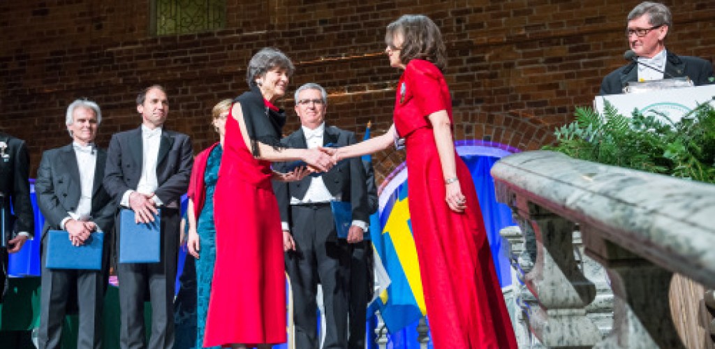 A woman shakes hands with another woman on stage at a recognition ceremony