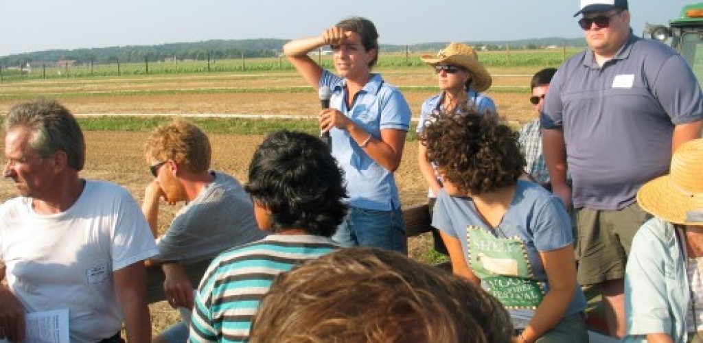 A group of people stand outside listening to a woman speak into a microphone