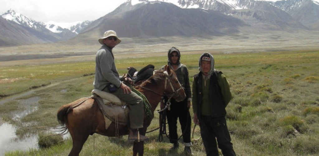 One man sits on horseback while two men stand besides him in the Pamir Mountains of Afghanistan