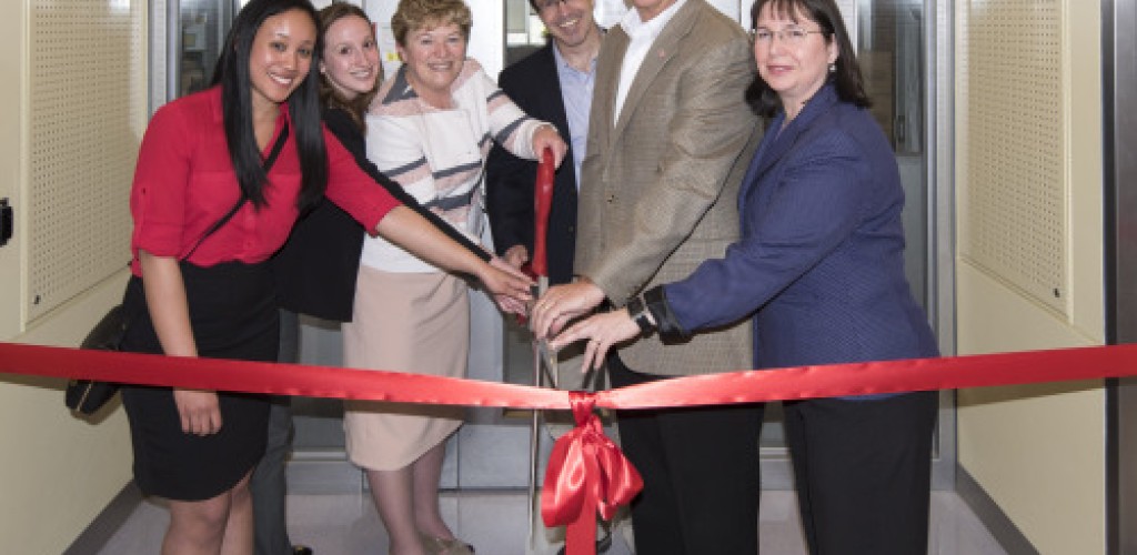 A group of people cut a red ribbon in front of a new facility for food safety research