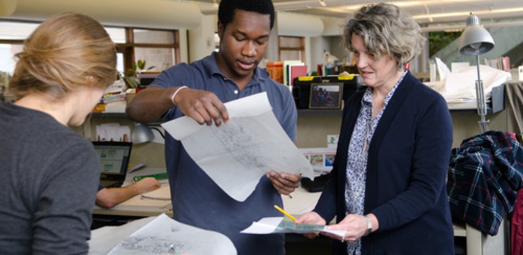 Three people hold and look at papers inside a studio