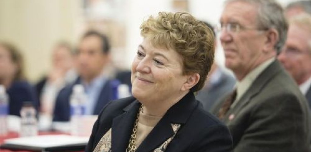 A woman in focus sits in front of a crowd of people who are blurred in the background