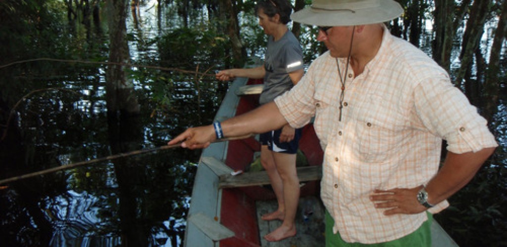 A man and a woman stand in a boat on a river with fishing rods in the water