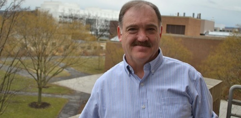 A man stands outside with Cornell campus buildings in the distance
