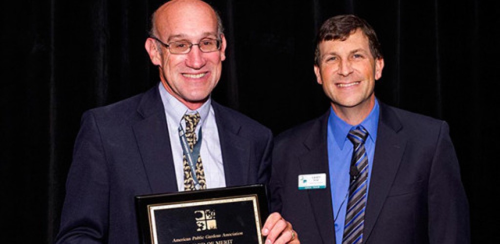 Two men stand together and hold an award