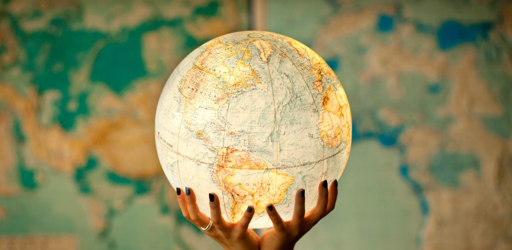 Two hands hold a globe in front of a map of the world