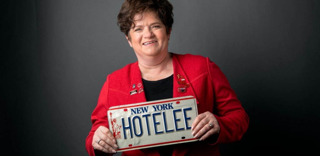 A woman in Cornell jacket presents a license plate that reads "HOTELEE"