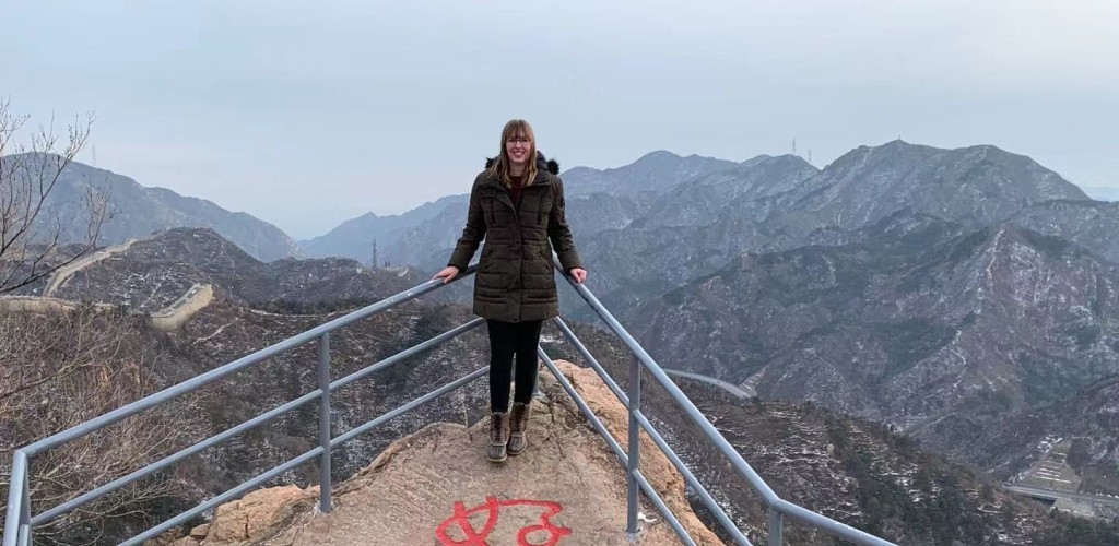 a college-aged woman stands by a railing on the Great Wall of China