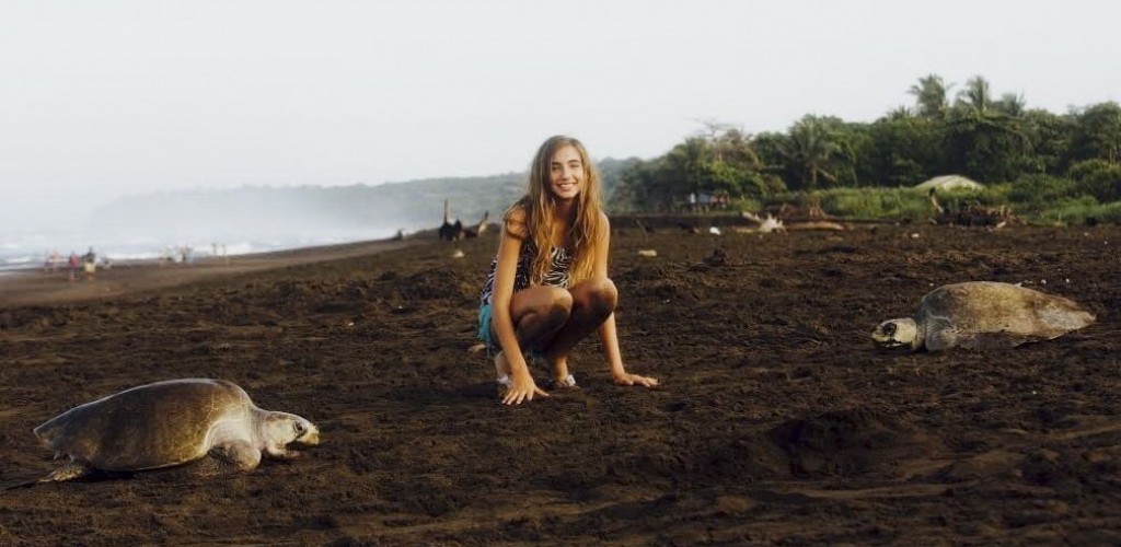 A girl on the beach crouching between two large sea turtles 