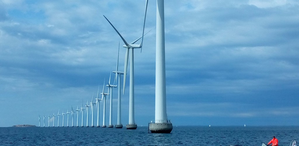 large wind turbines in the middle of the ocean with a boat floating nearby