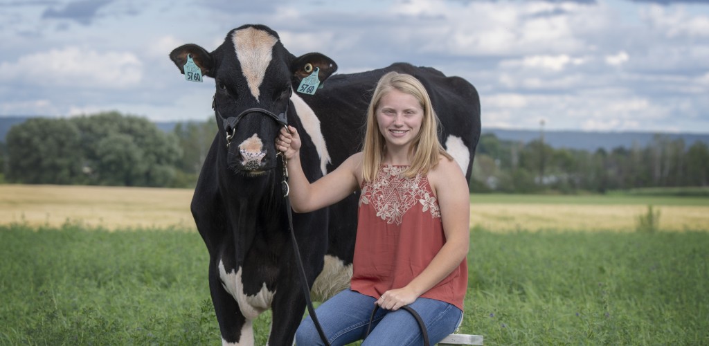 Rachel sitting on a stool outside holding onto a cow's bridal