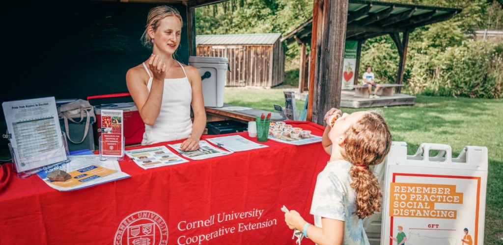  Ainsley Fleming-Wood offers food to a child at a farmers market booth for Cornell Cooperative Extension