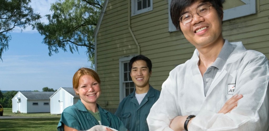 Xingen Lei standing with students outside. One student holds a piglet 
