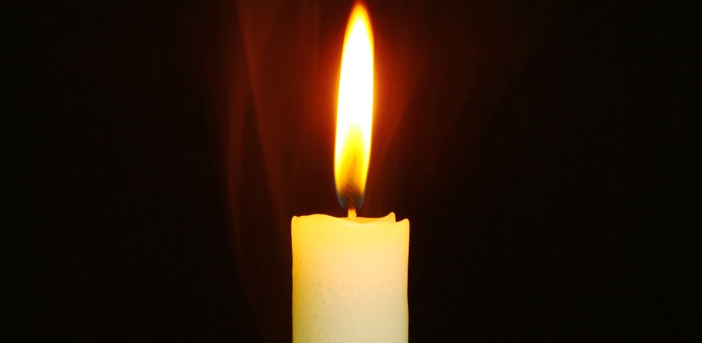 A lit candle infront of a dark background.