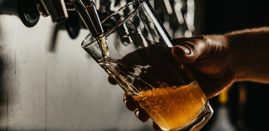 A hand pouring a glass of beer from a bar tap.