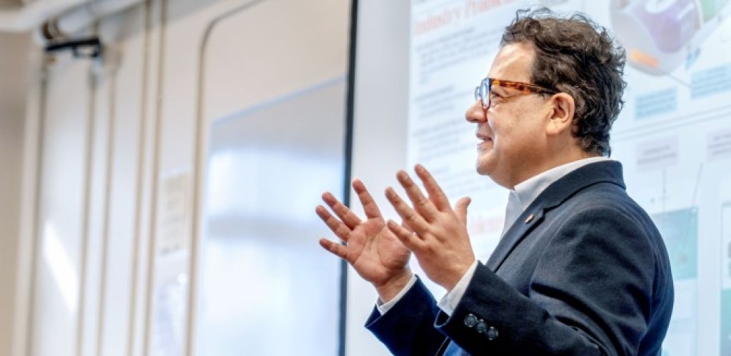 Juan Hinestroza speaking in front of a projecter screen. 