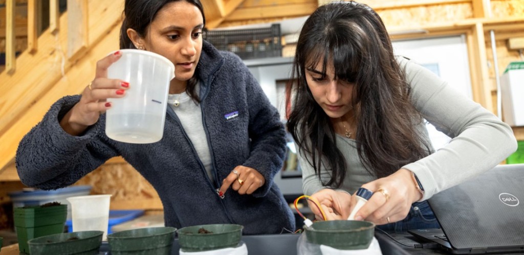 Two female students hold plastic containers and examine circuitry. 