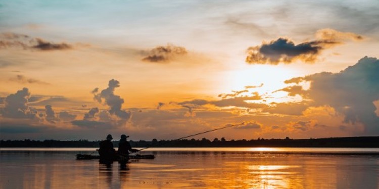 Two fisherman on a small boat cast fishing lines into the water at sunset